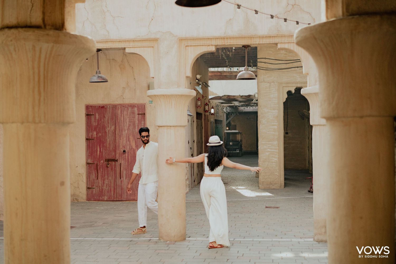 Couple in white outfits dancing in an arched courtyard with sandy stone columns at a destination wedding venue.