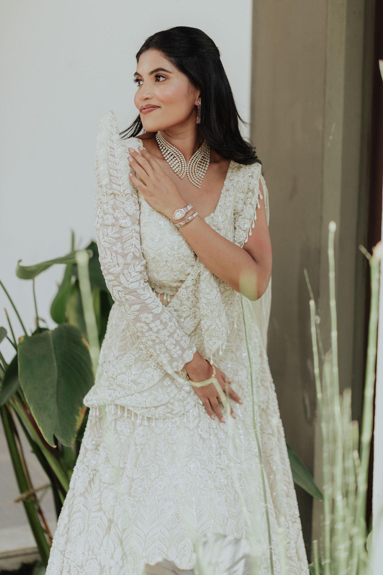 Bride in elegant white embroidered lehenga with pearl choker necklace and bangles posing gracefully outdoors.