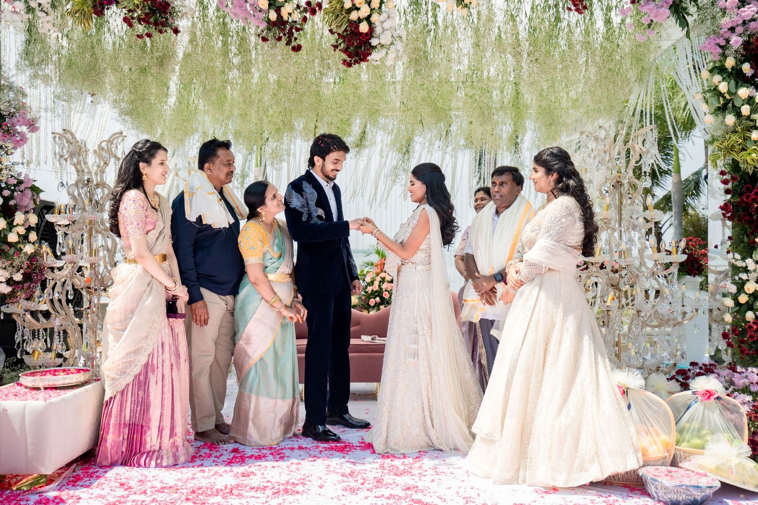 Indian wedding ceremony with couple exchanging vows under floral canopy surrounded by family members.