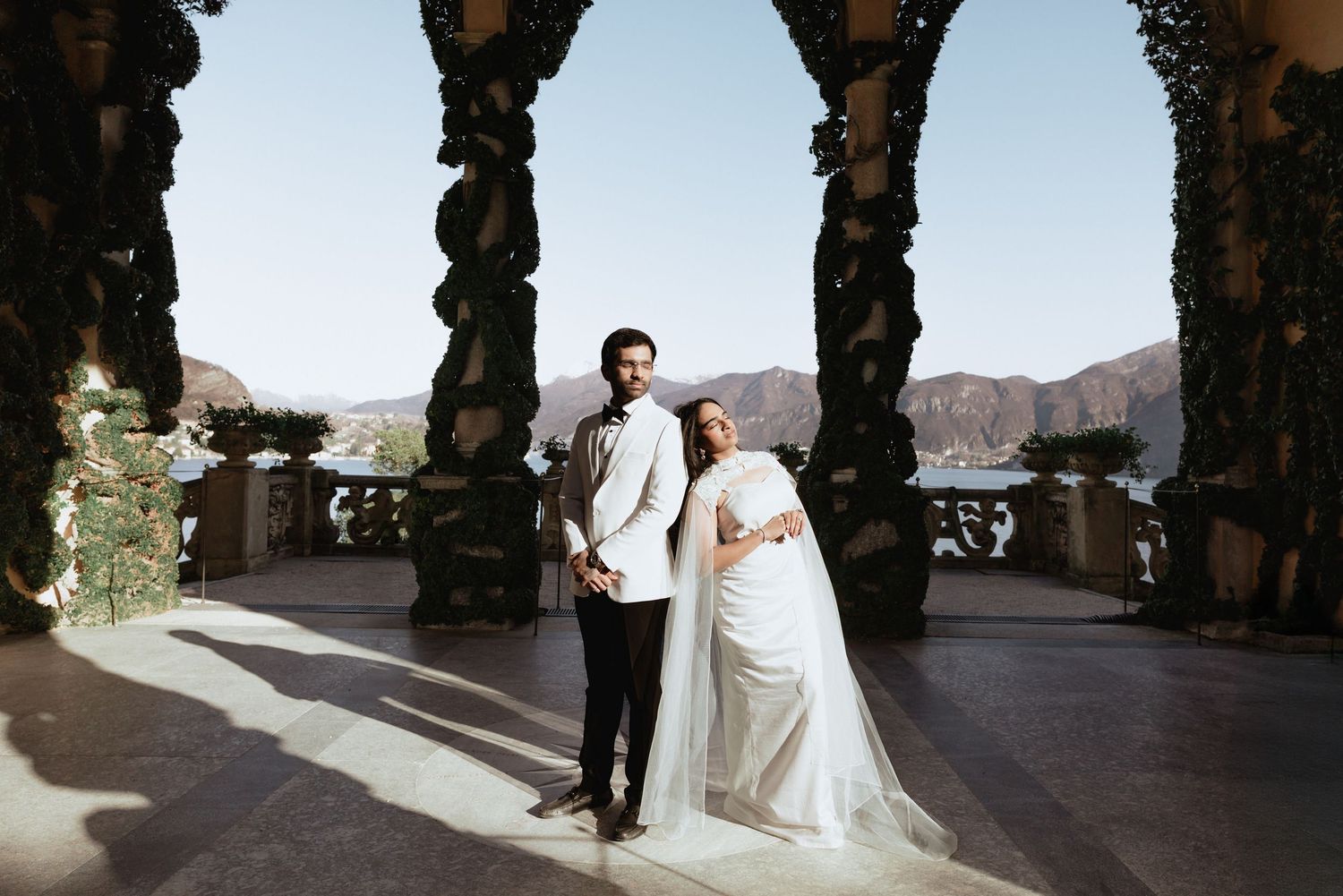 Elegant bride and groom pose on a scenic terrace with mountain views on their wedding day.
