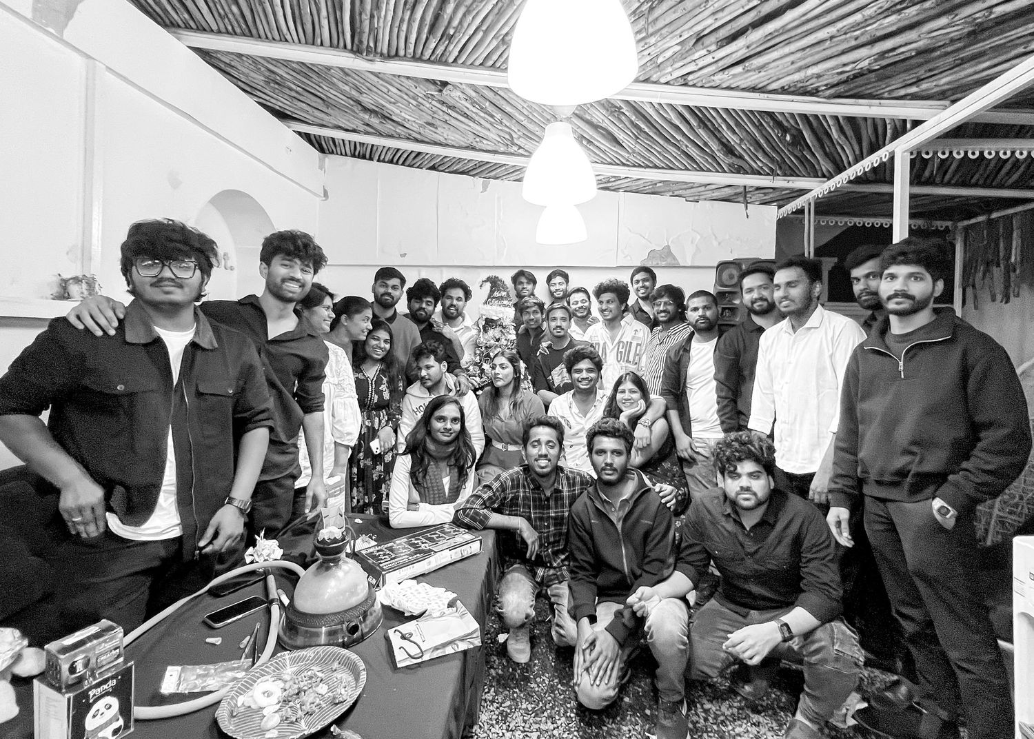 Large group of young people posing together indoors under a thatched roof ceiling for a group photo.
