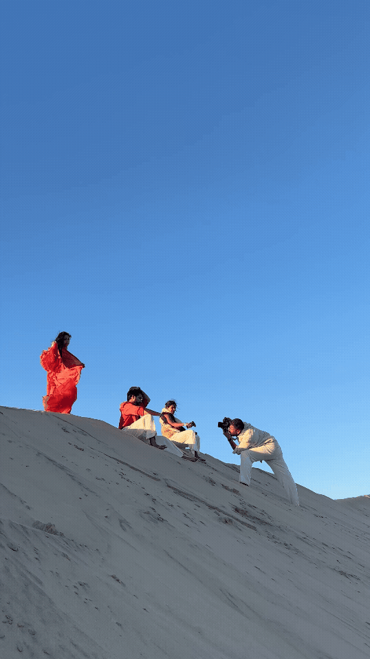 People in colorful outfits pose and photograph on a white sand dune under a clear blue sky.