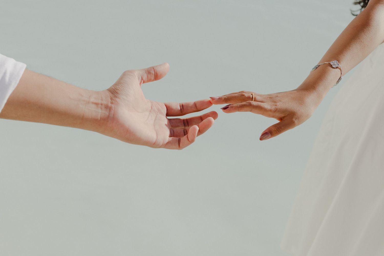 Two hands reaching toward each other against a light background, symbolizing connection and unity.