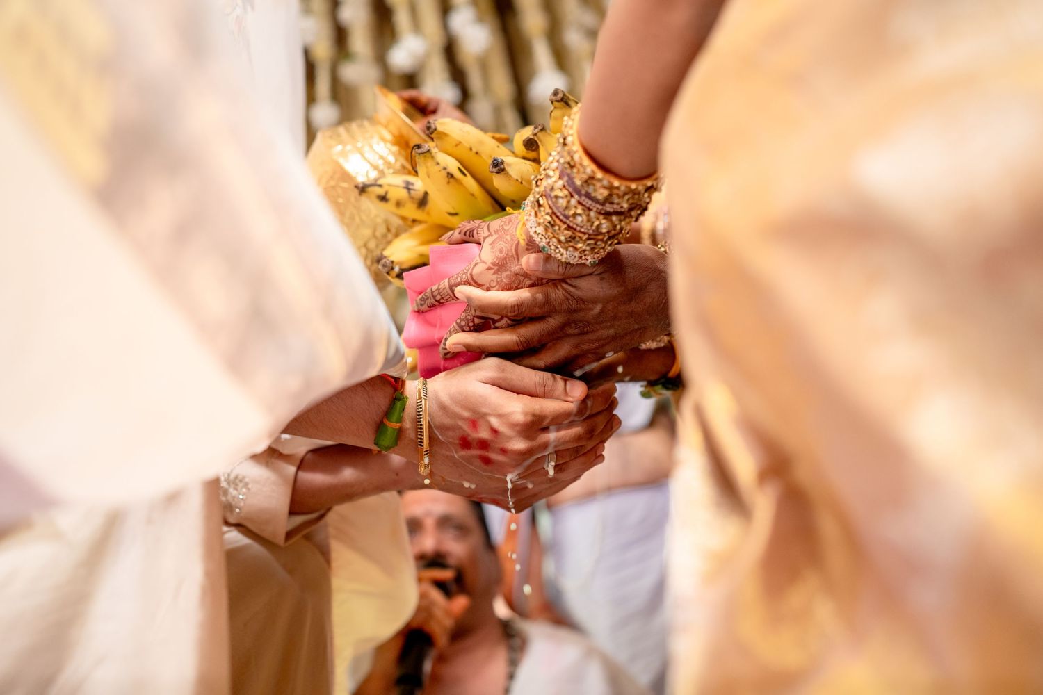 Close-up of a Hindu wedding ritual with hands exchanging flowers adorned with gold bangles and mehndi.