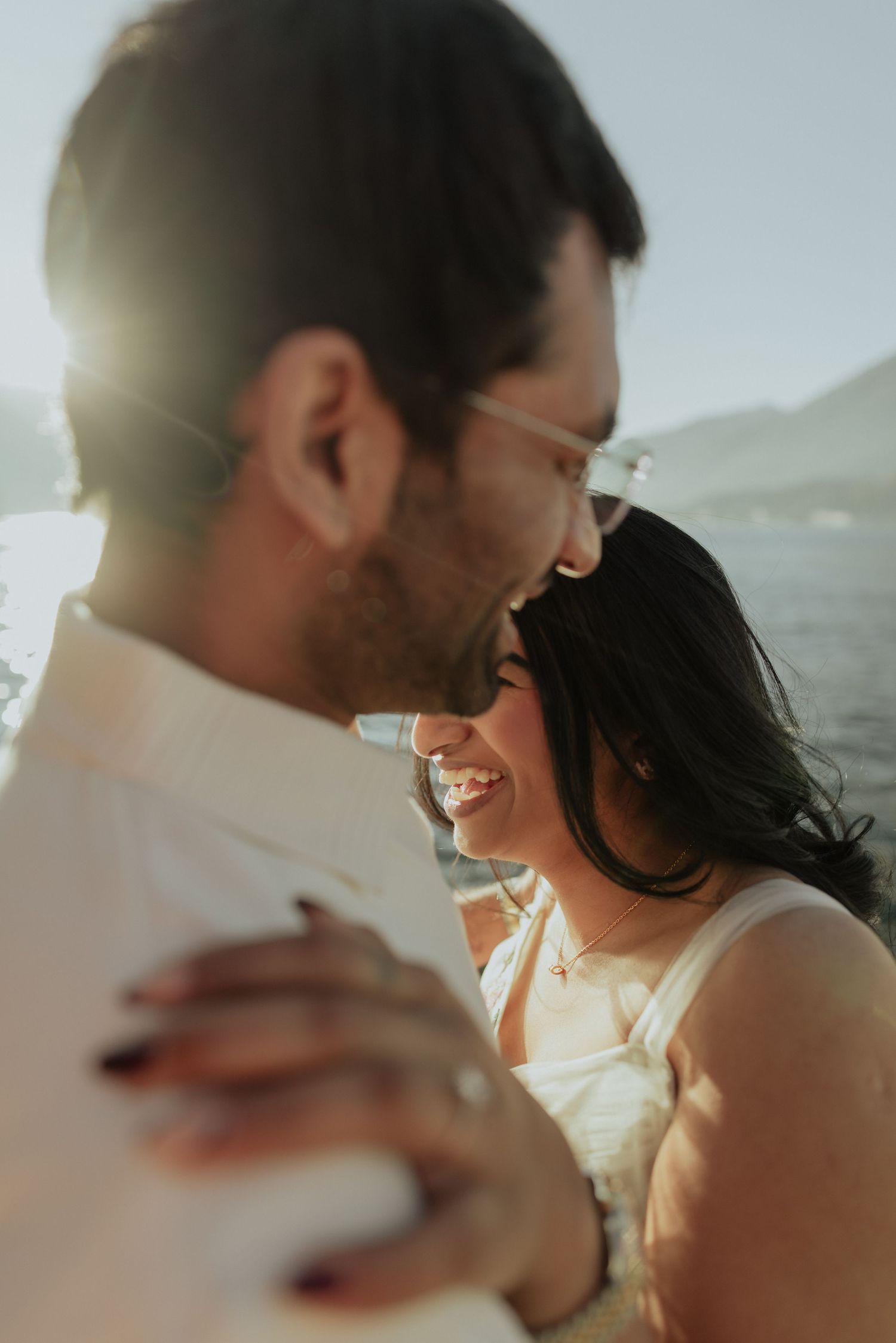 Couple sharing a joyful moment close together with sunlight glowing behind them near a lake.