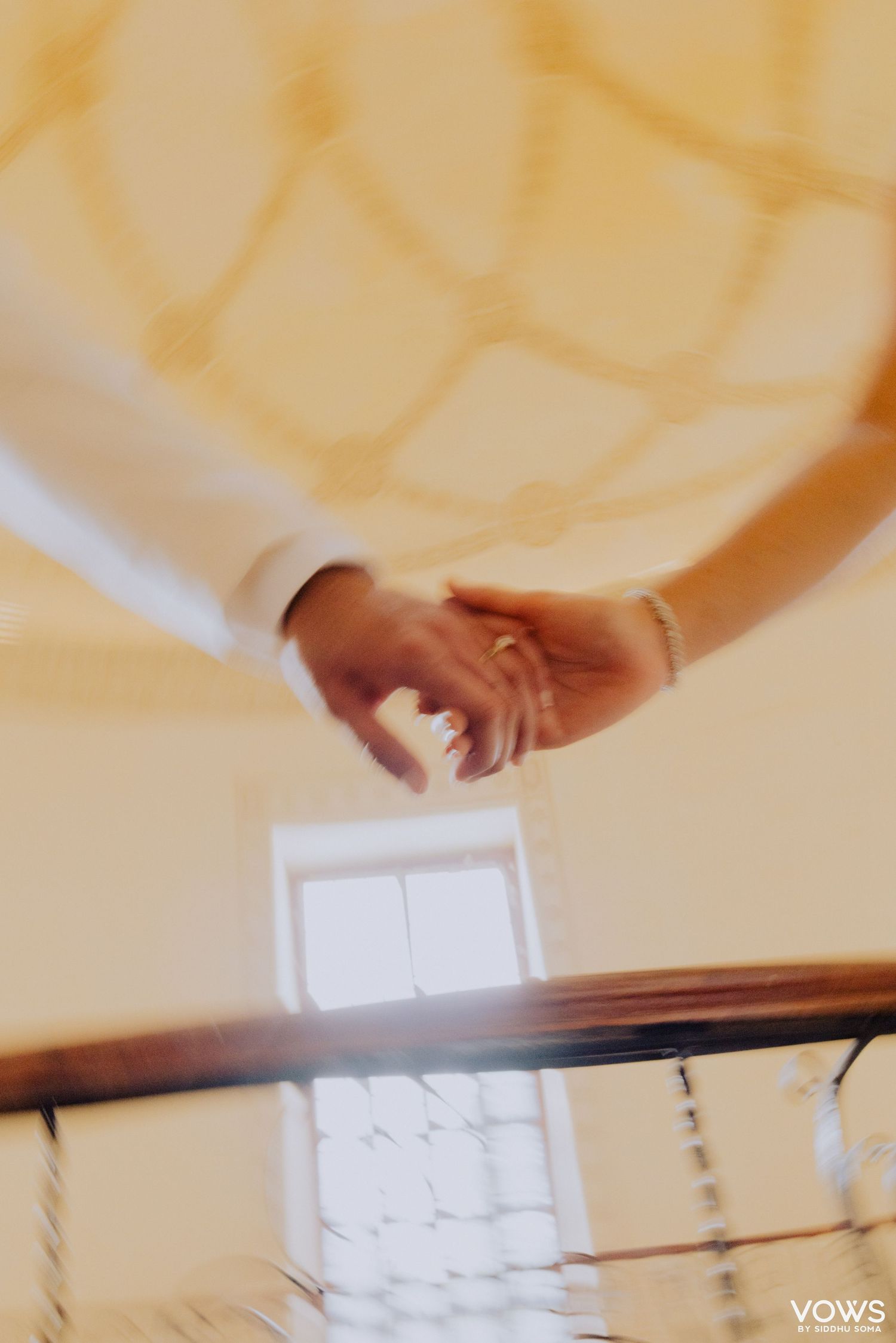 Couple holding hands on a staircase railing, wearing wedding attire with a gold bracelet visible.
