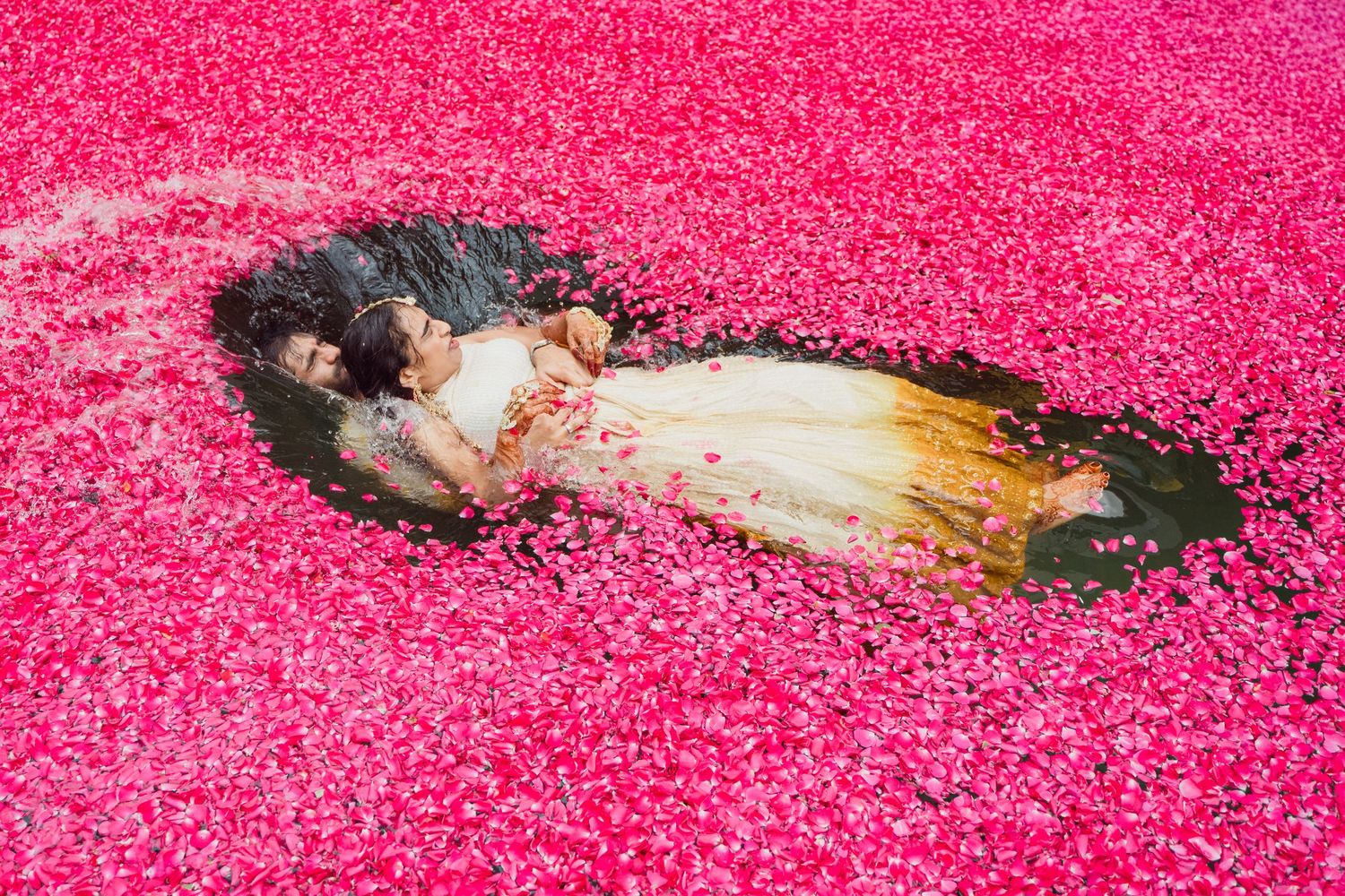 A woman in a white dress lies surrounded by vibrant pink rose petals in a stunning artistic photo.