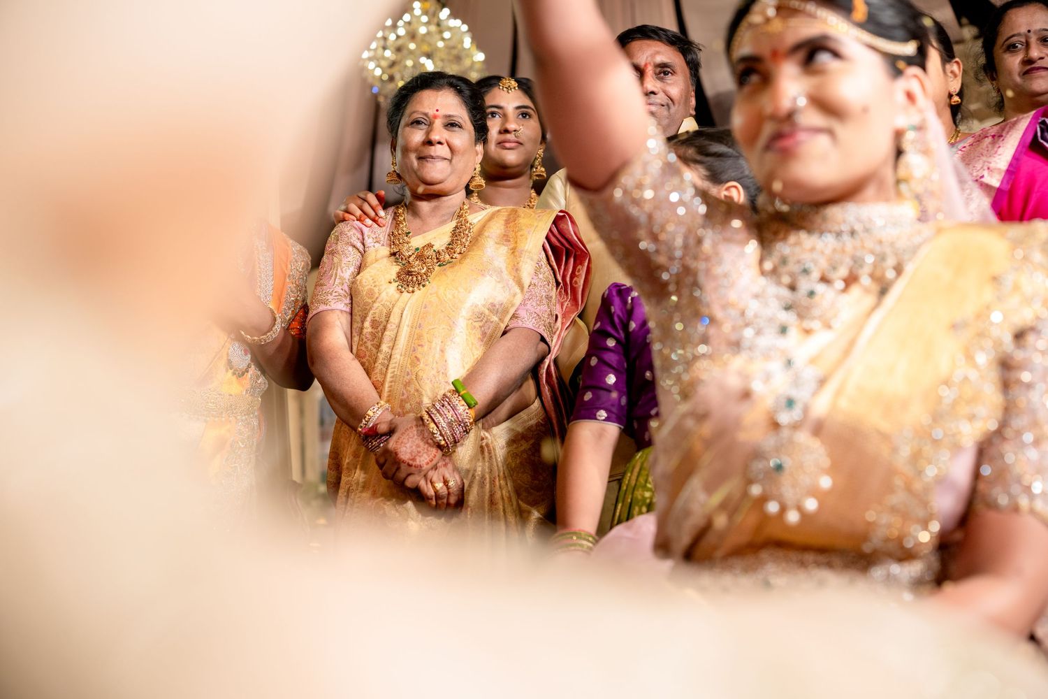 An emotional mother watches her daughter during a traditional South Indian wedding ceremony in golden sarees.