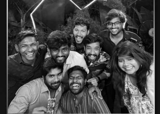 Black and white group photo of eight smiling young friends posing together at an outdoor evening event.