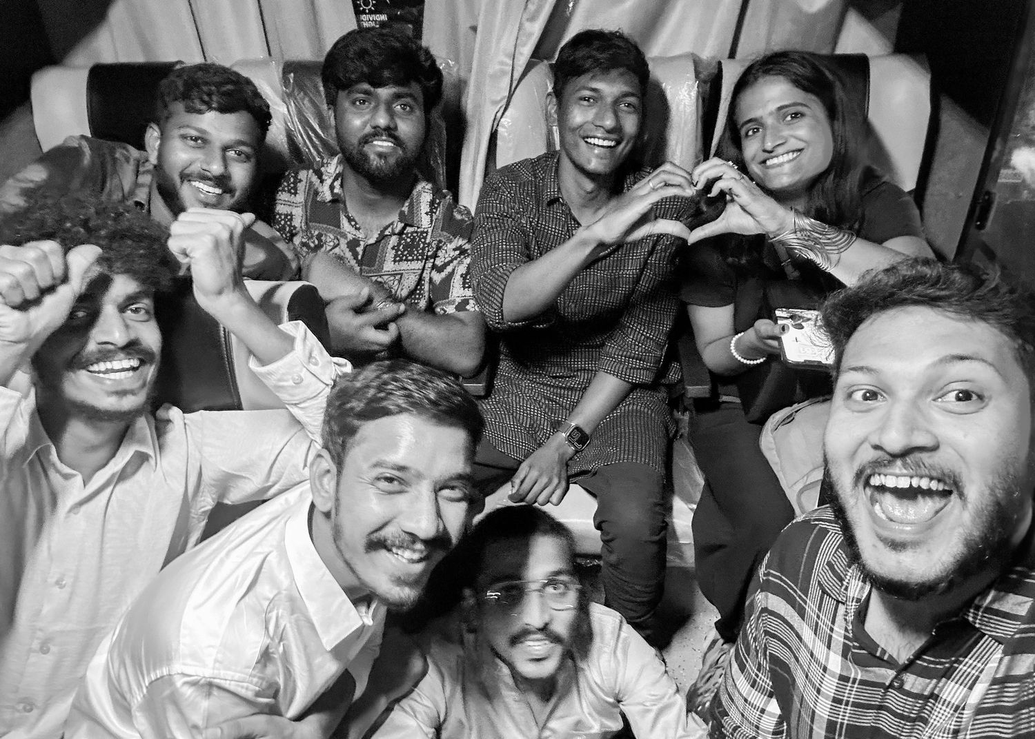 Black and white group photo of eight smiling friends posing together indoors, making heart gestures.