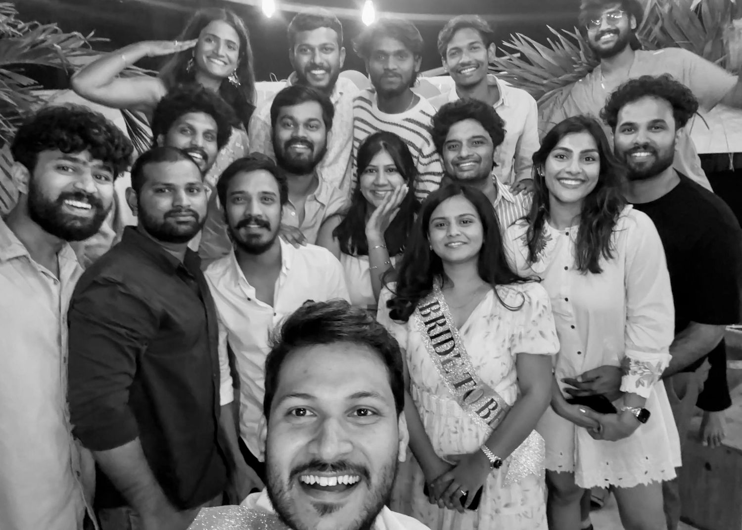 Black and white group selfie of friends smiling at a casual outdoor gathering, one woman wearing a sash.