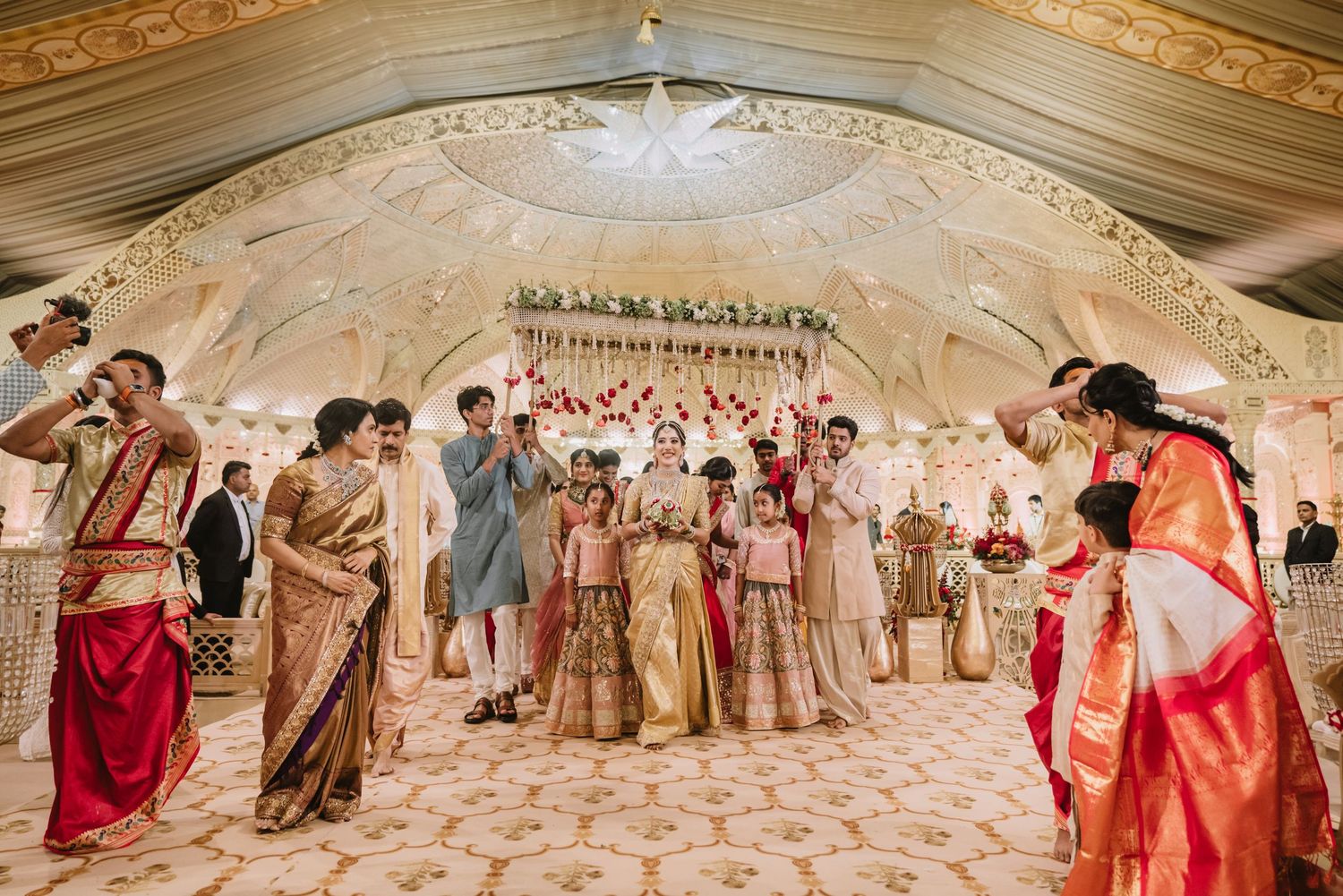Guests in vibrant traditional Indian attire celebrate at an elegant wedding ceremony in a beautifully decorated banquet hall.