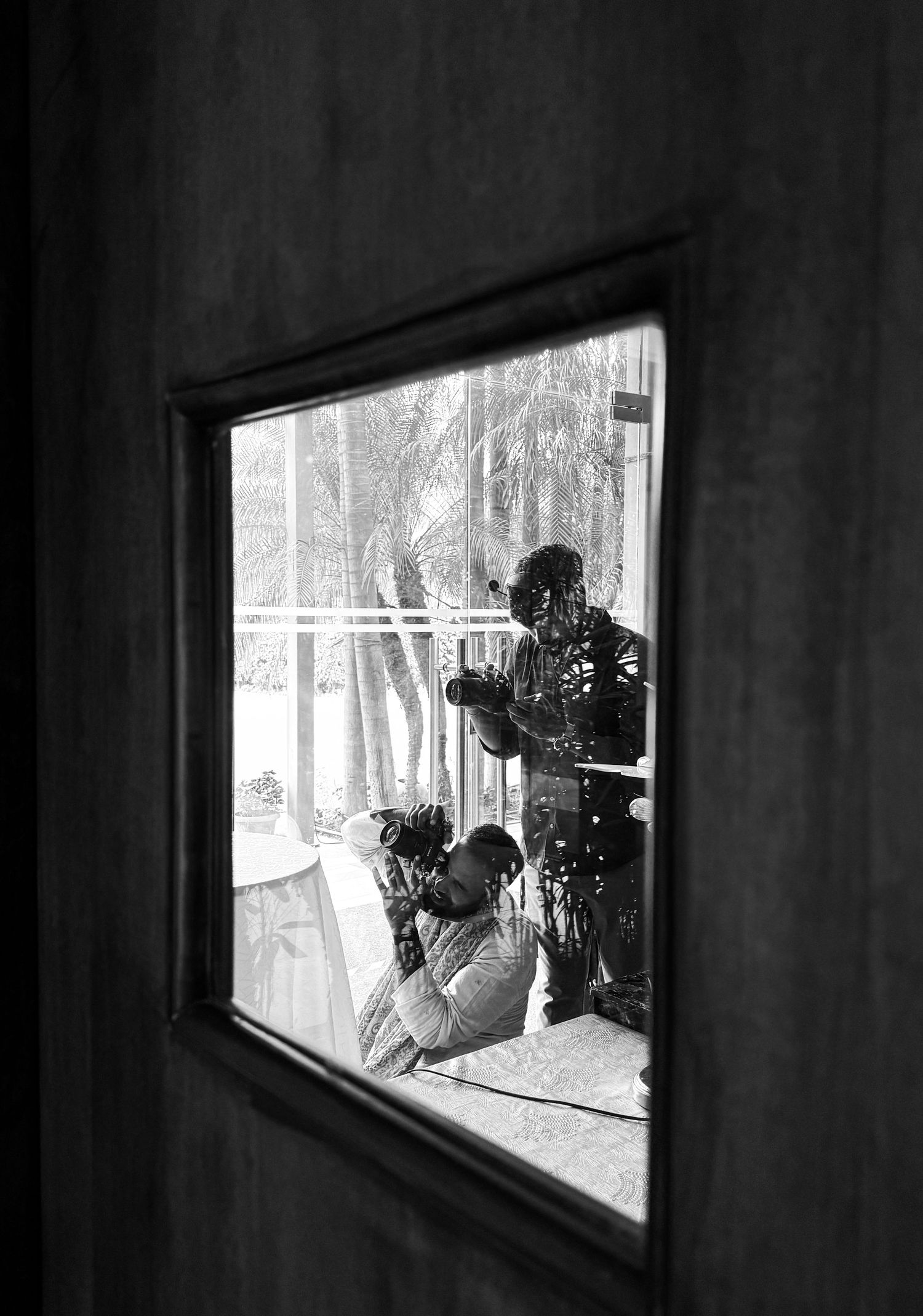 Black and white photo of two photographers shooting through a small square window on a tropical balcony.