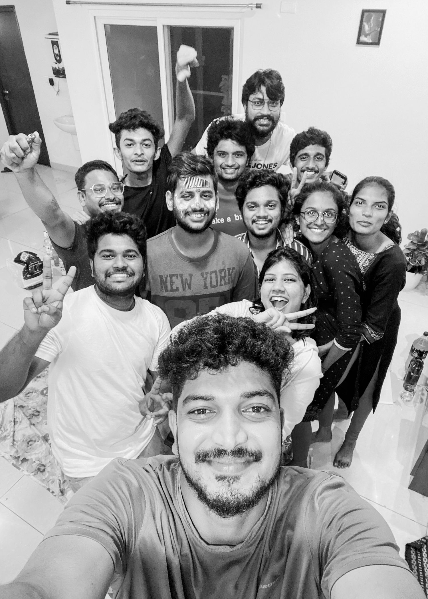 A group of young friends taking a fun black and white selfie together indoors, smiling and posing happily.