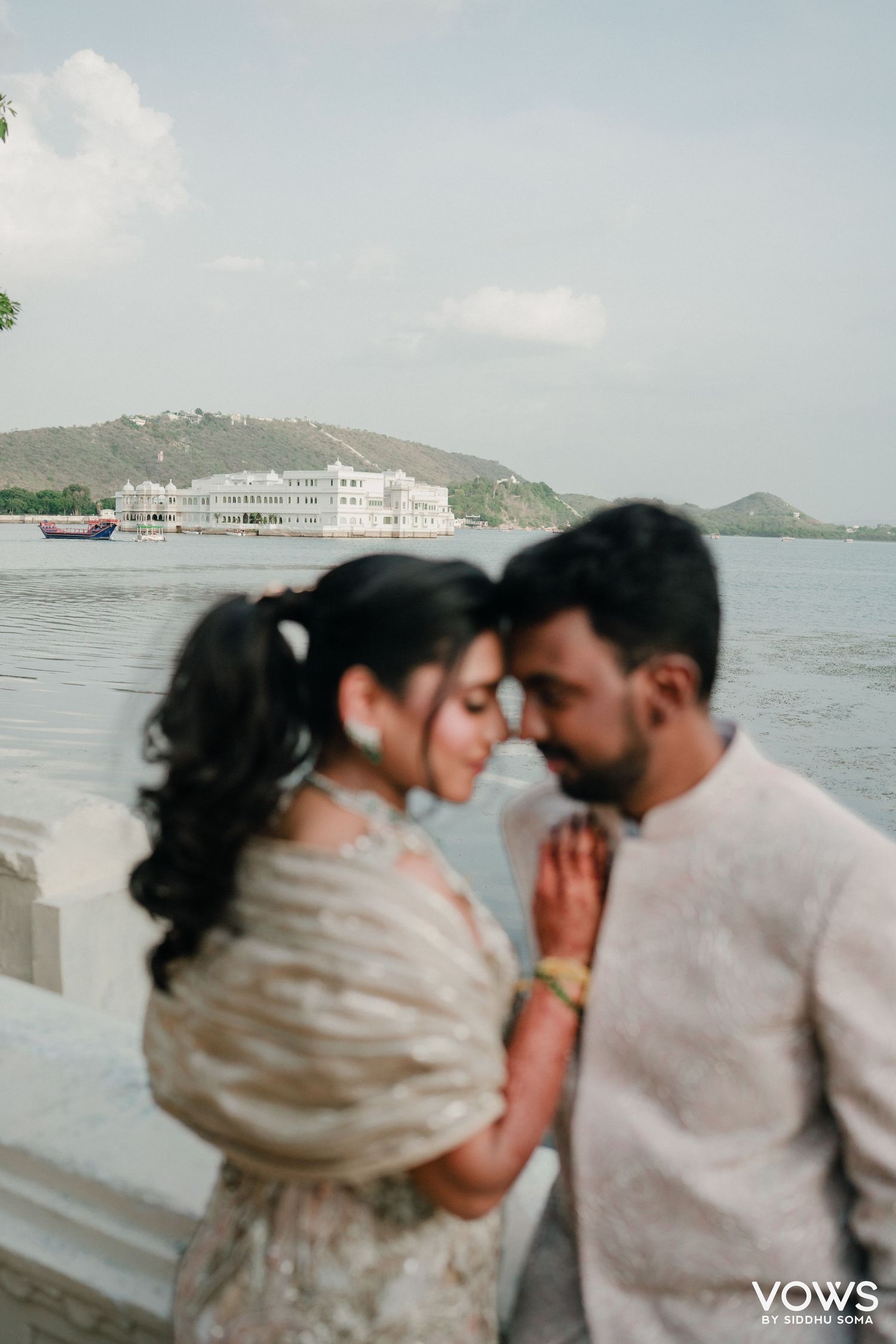 Romantic couple shares intimate moment by Lake Pichola with Lake Palace in background, Udaipur, India.