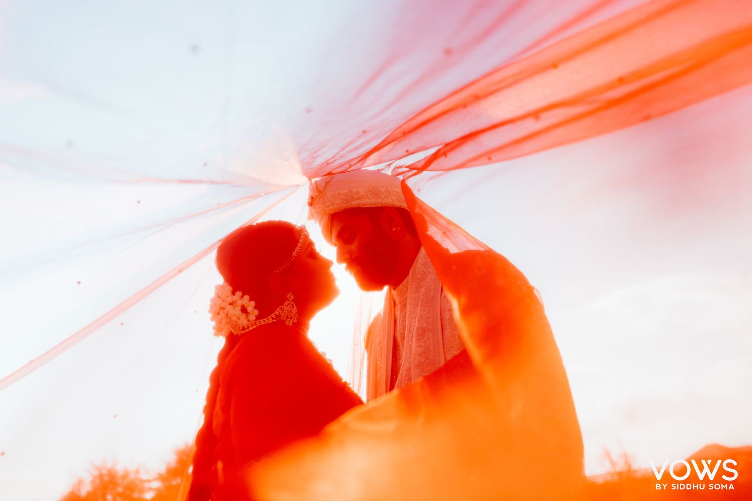 Romantic silhouette of a couple under a flowing red veil at their wedding ceremony.