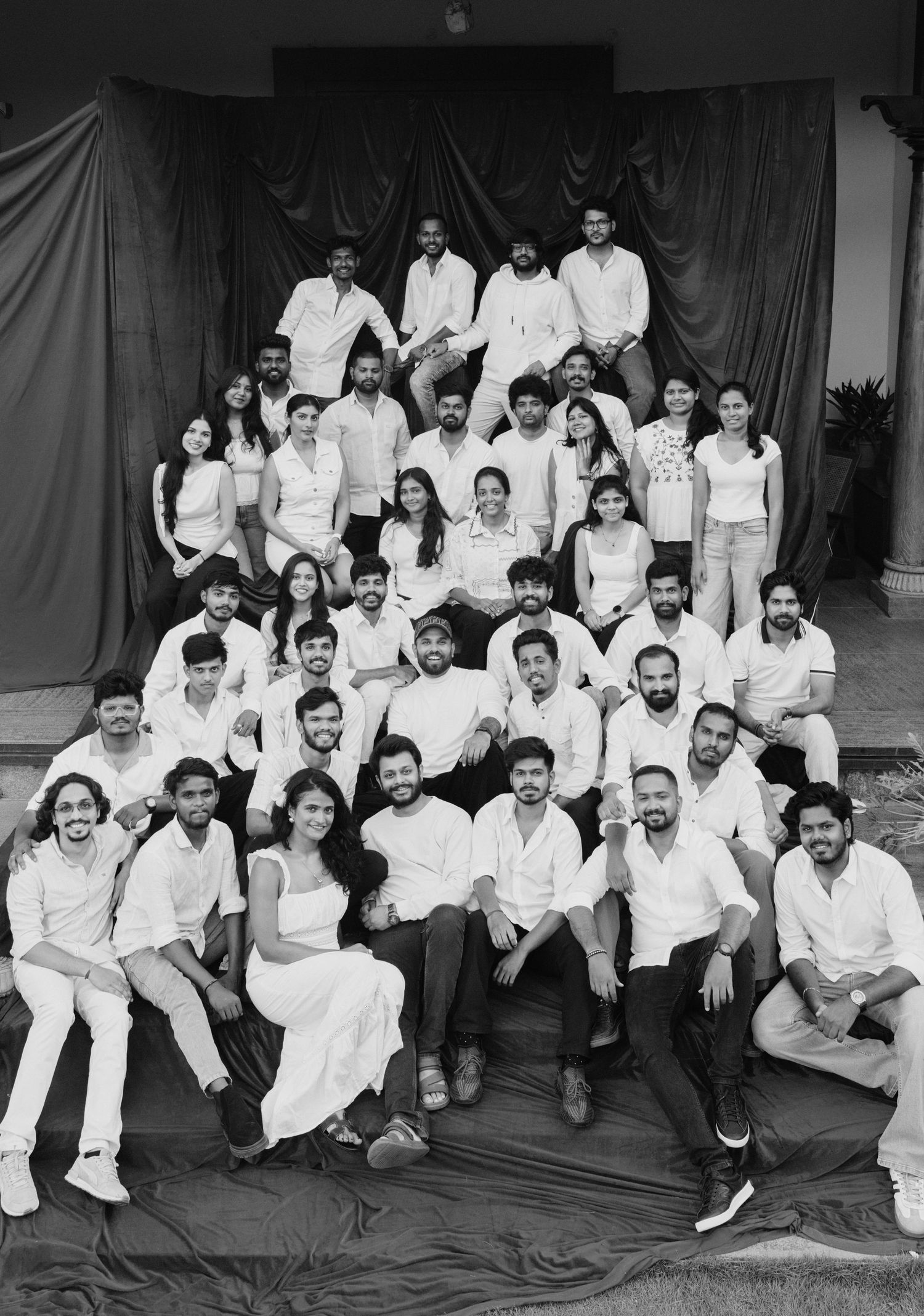 Black and white group photo of approximately 40 young adults dressed in white, posed on outdoor steps.