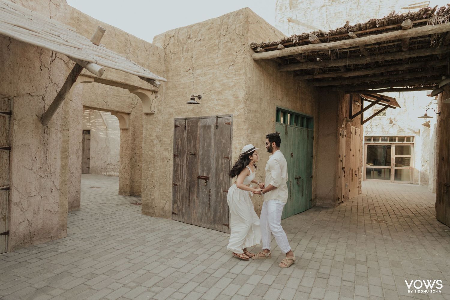 Couple dancing in a rustic Middle Eastern courtyard with sandy walls and wooden doors, captured by Vows Photography.
