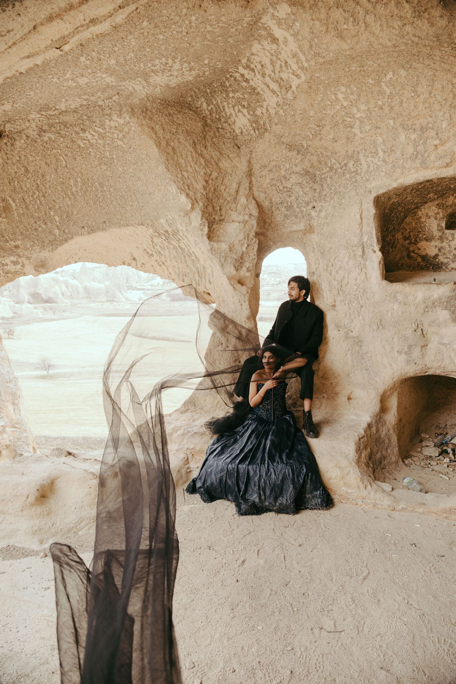 Couple in black outfits posing in a cave dwelling in Cappadocia, Turkey, with flowing black tulle fabric.