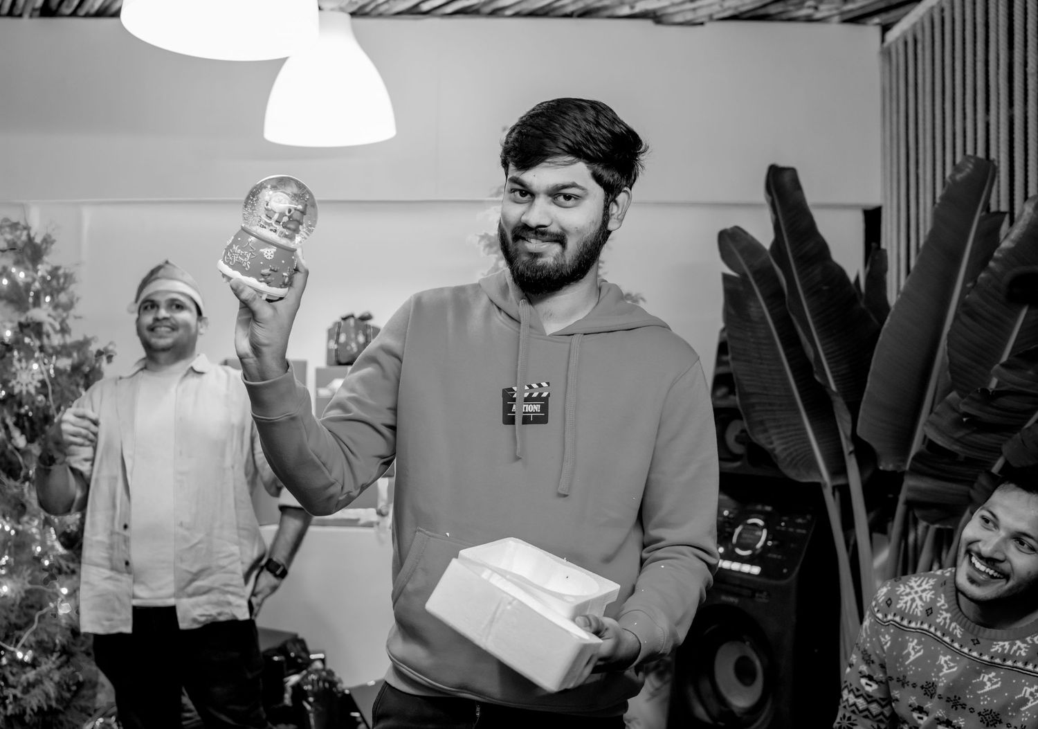 Man smiling holding gift and snow globe at festive Christmas party in black and white photo.