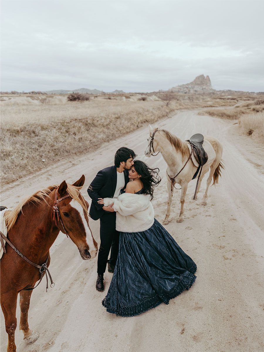 Couple embraces romantically on a dirt road surrounded by horses in a rustic outdoor elopement setting.