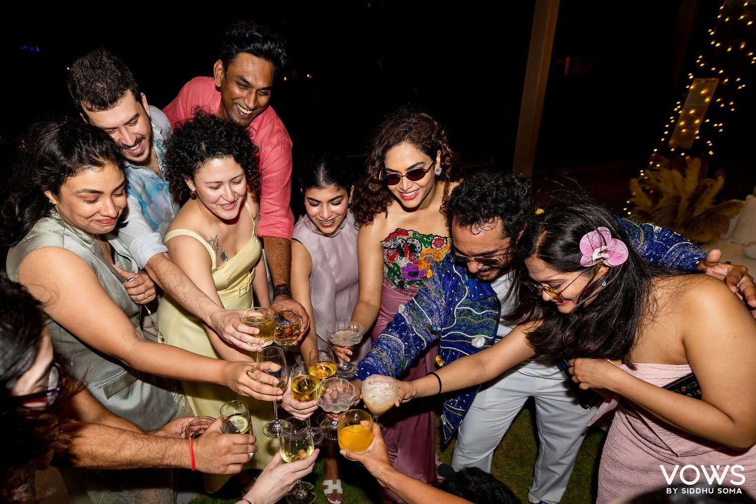 A joyful group of friends toasting drinks together at a festive outdoor night celebration.