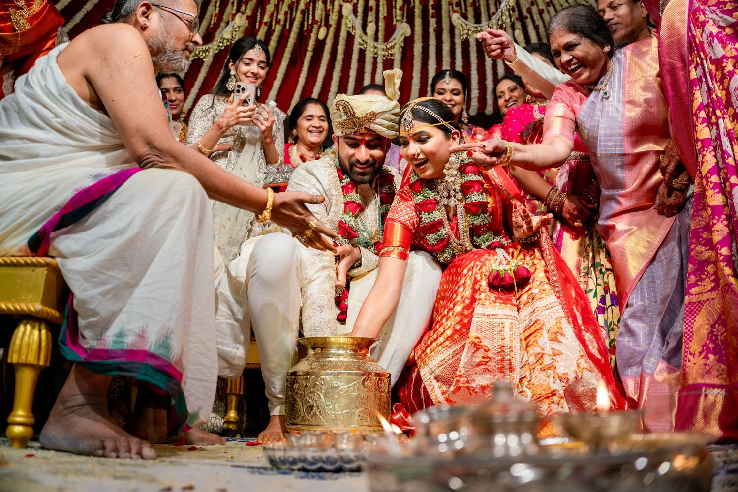 Vibrant Indian wedding ceremony with bride in red lehenga and groom in white sherwani surrounded by family performing rituals.