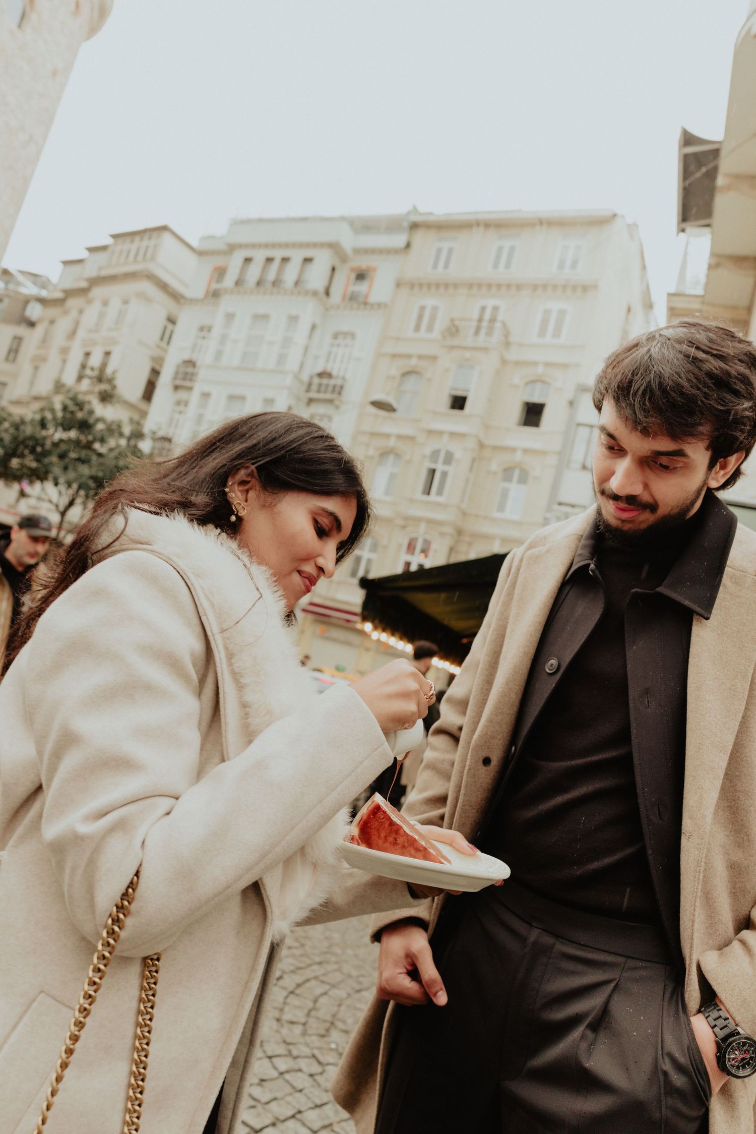 Couple sharing street food together in a European city square during winter.