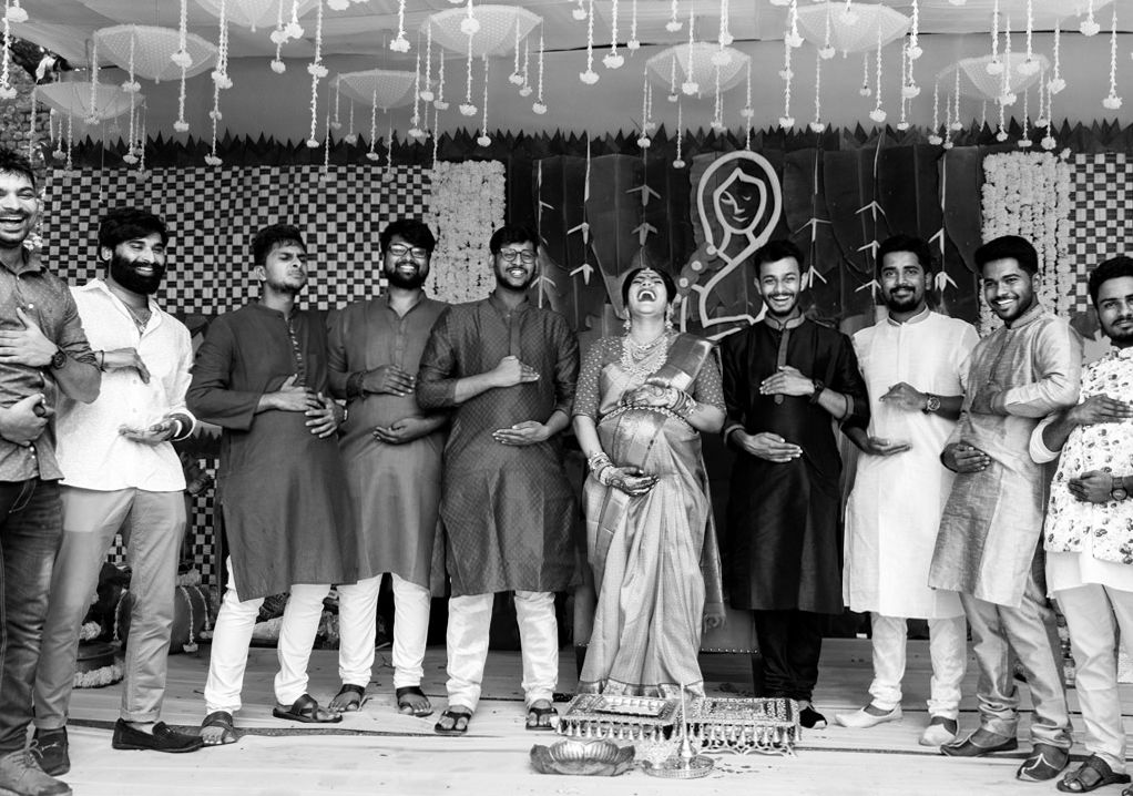 Black and white photo of a group posing at an Indian wedding celebration with floral decorations.