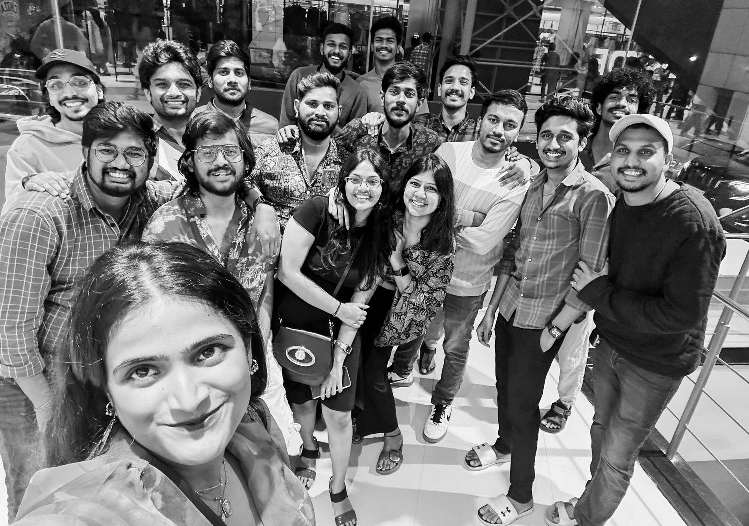 Black and white selfie of a large group of young adults posing together indoors at a social gathering.