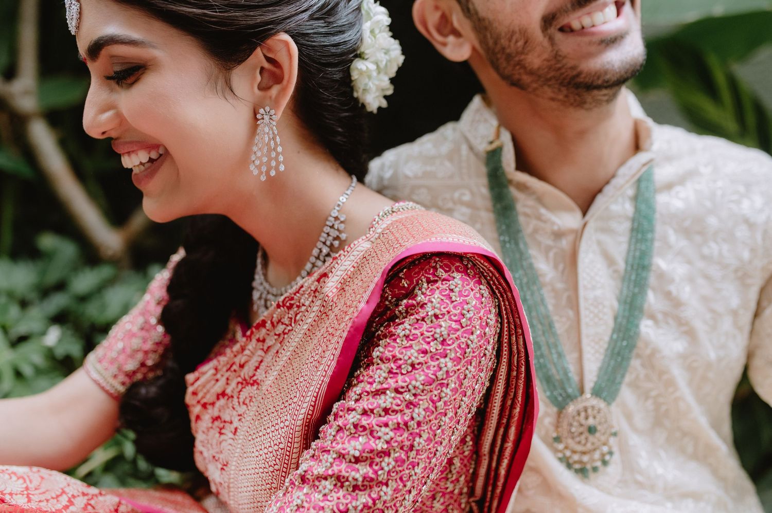 Smiling Indian couple in traditional wedding attire, bride in pink saree with floral hair accessory and groom in kurta.