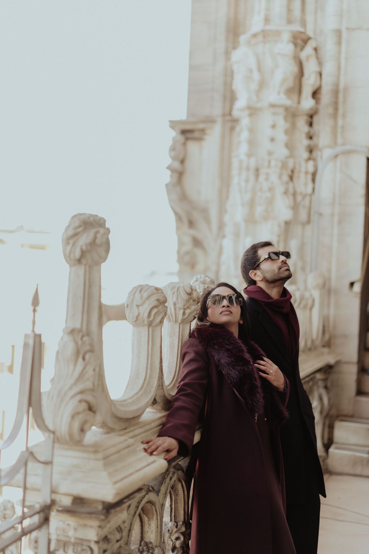 Stylish couple in burgundy and black coats posing on the rooftop terrace of Milan's Duomo.