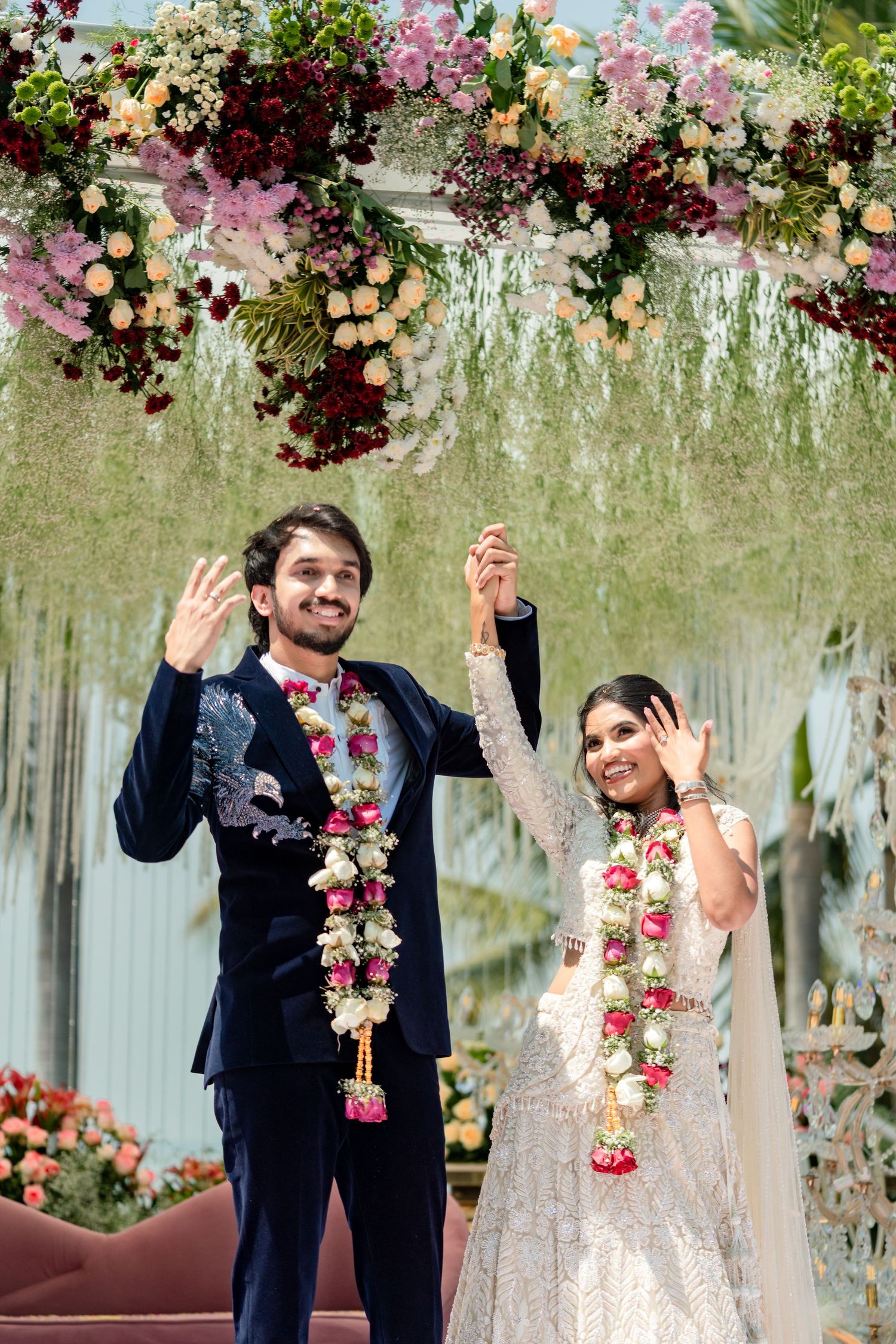 Newlyweds in traditional Indian attire celebrating under floral wedding mandap.