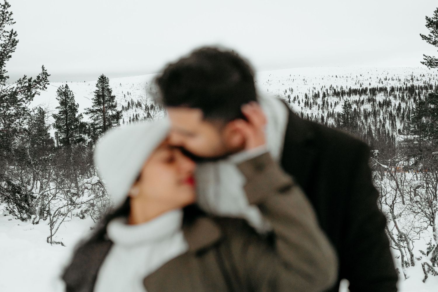 Couple sharing a romantic kiss in a snowy winter landscape surrounded by frost-covered trees.