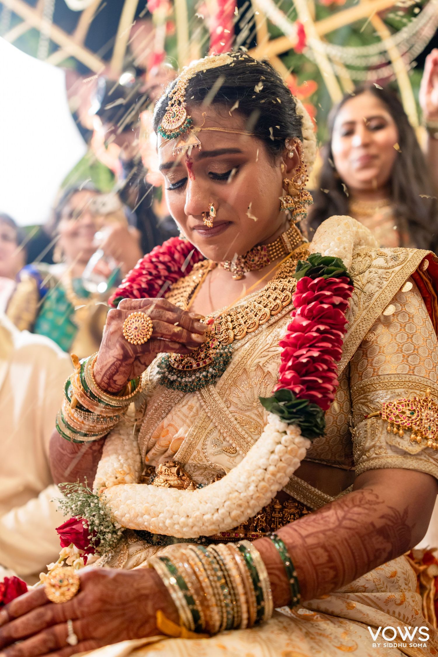 A South Indian bride in gold silk saree with floral garlands and traditional jewelry during wedding ceremony.