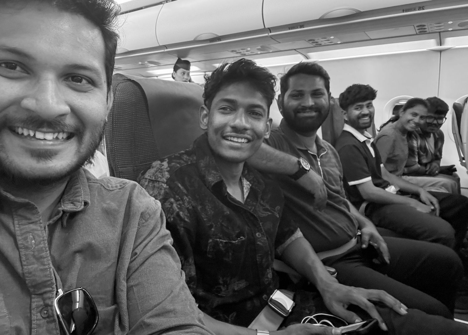 Group of young men smiling and taking a selfie together on an airplane in black and white photo.
