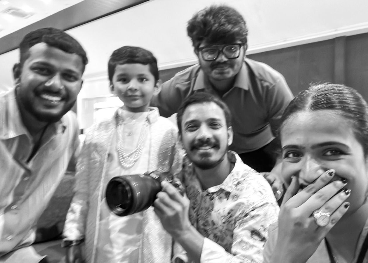 Black and white group selfie of five people, including a child in traditional attire, smiling at a camera.