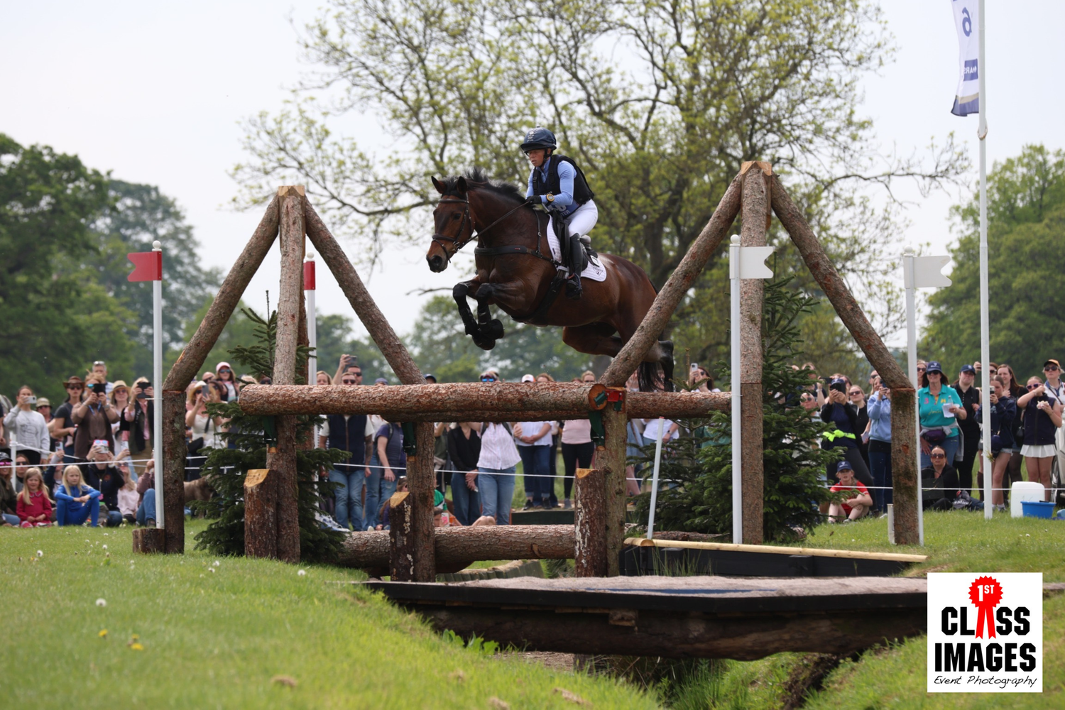 Rider on dark horse jumping large wooden cross-country fence at equestrian competition.