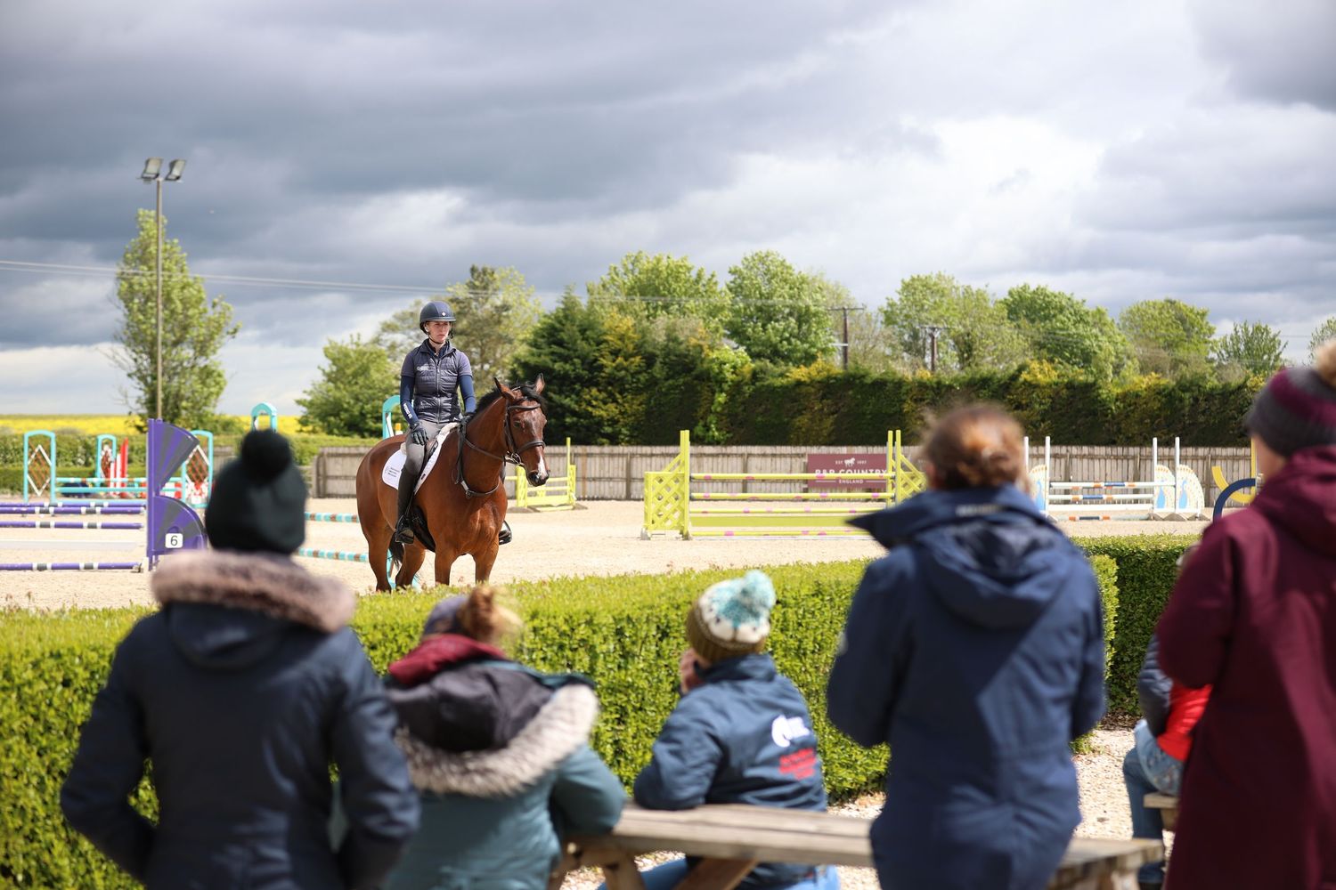 Rider on chestnut horse performing dressage while spectators watch at outdoor arena.