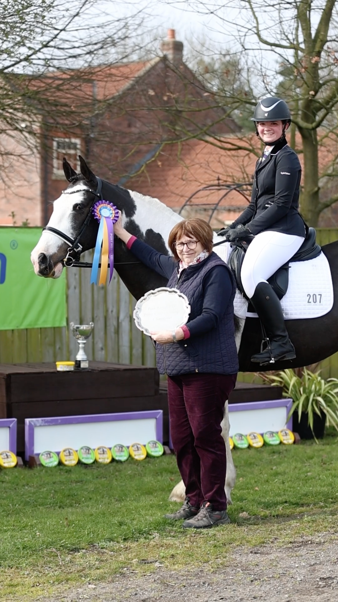 Award ceremony with a rider on a decorated pinto horse as a woman holds a silver trophy plate at an equestrian event.