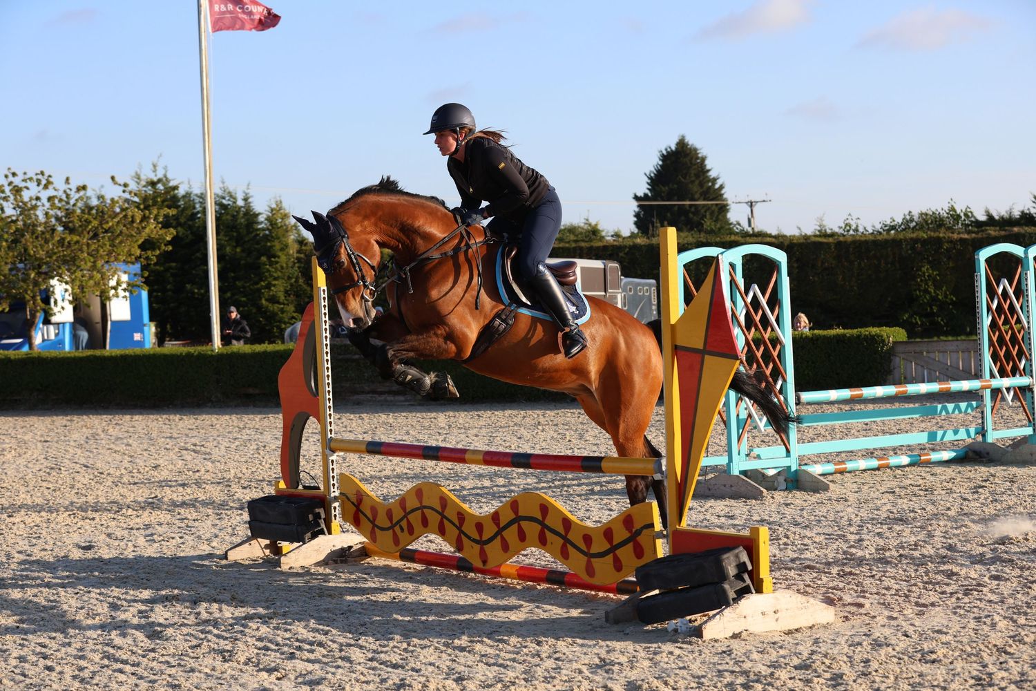 Bay horse and rider jumping a colorful fence obstacle in an equestrian show jumping competition.