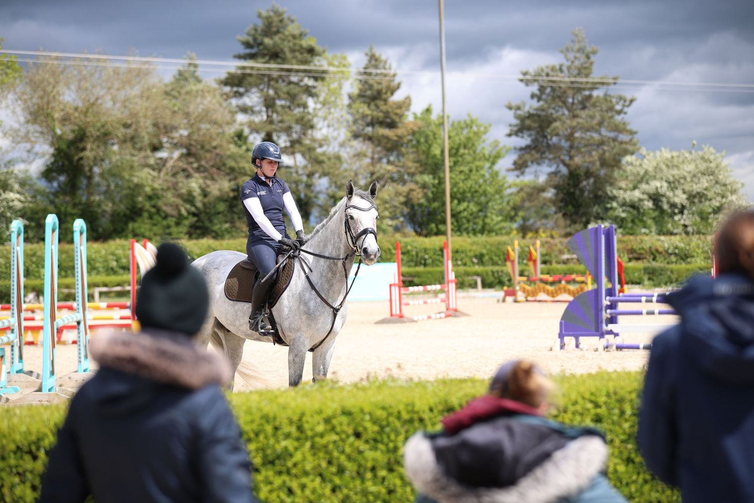 Rider on grey horse demonstrating equestrian skills to spectators at outdoor arena.