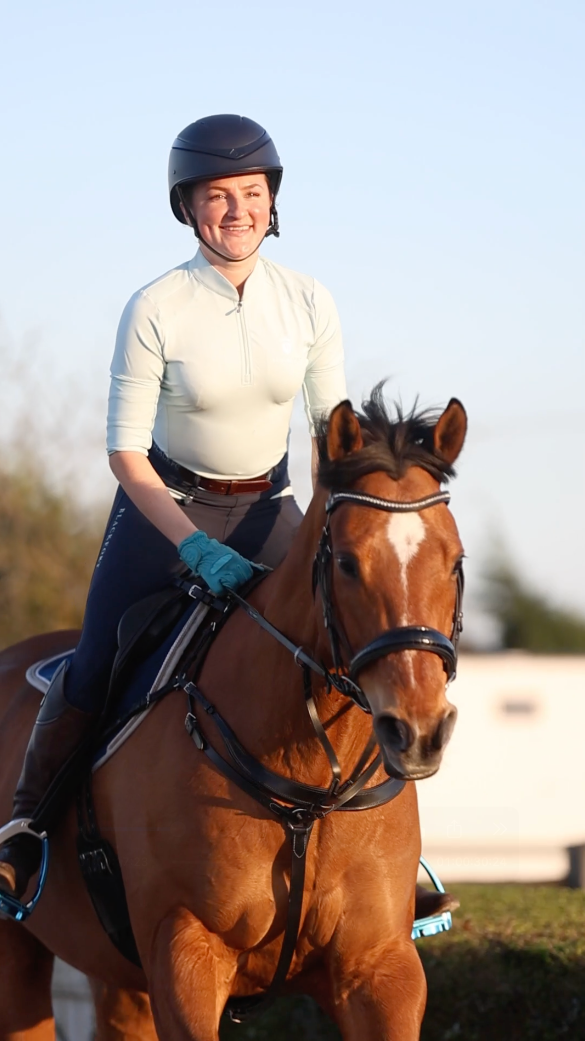 Smiling female equestrian rider on chestnut horse in golden evening light outdoors.