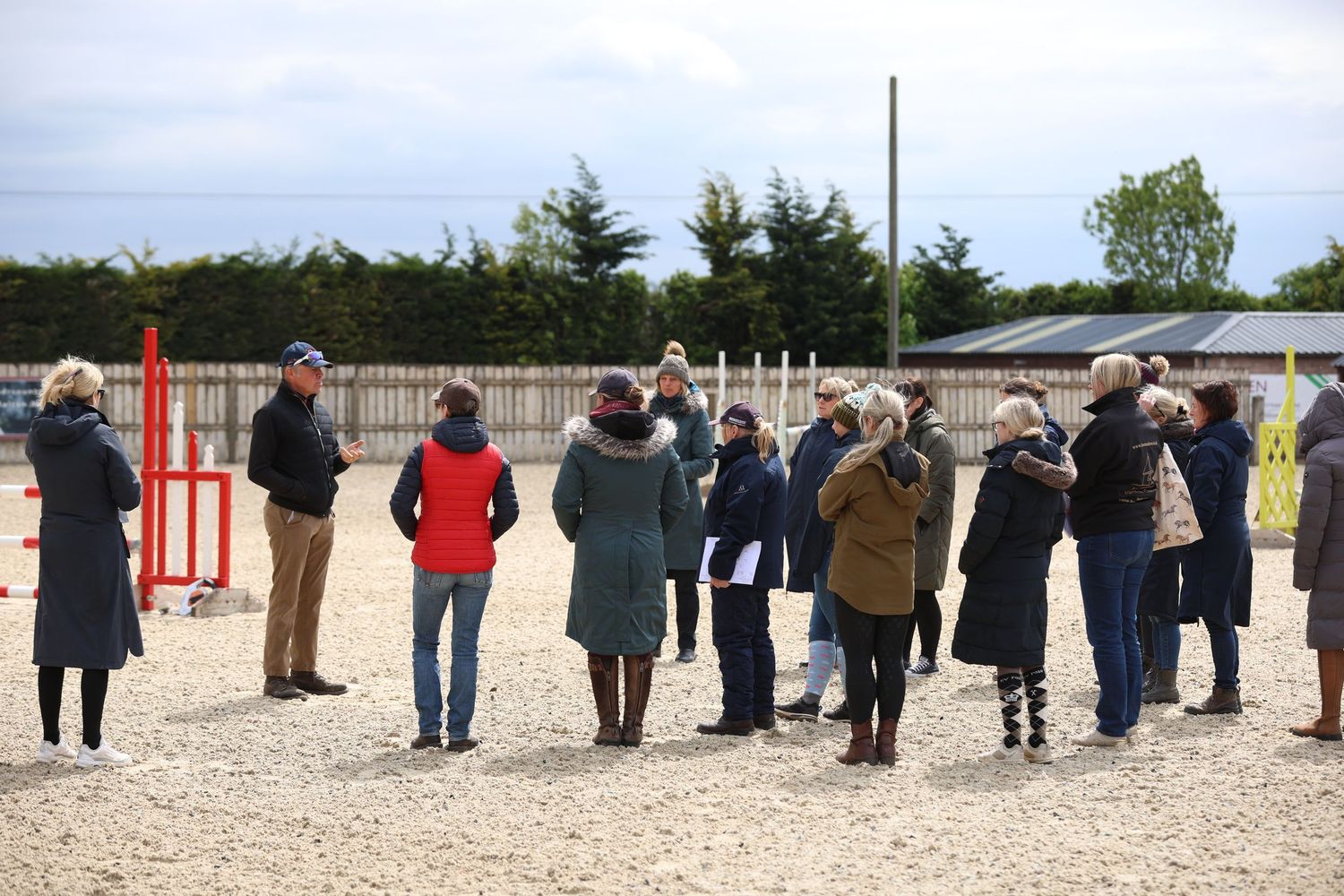 Group of spectators watching equestrian dressage training session at outdoor arena.