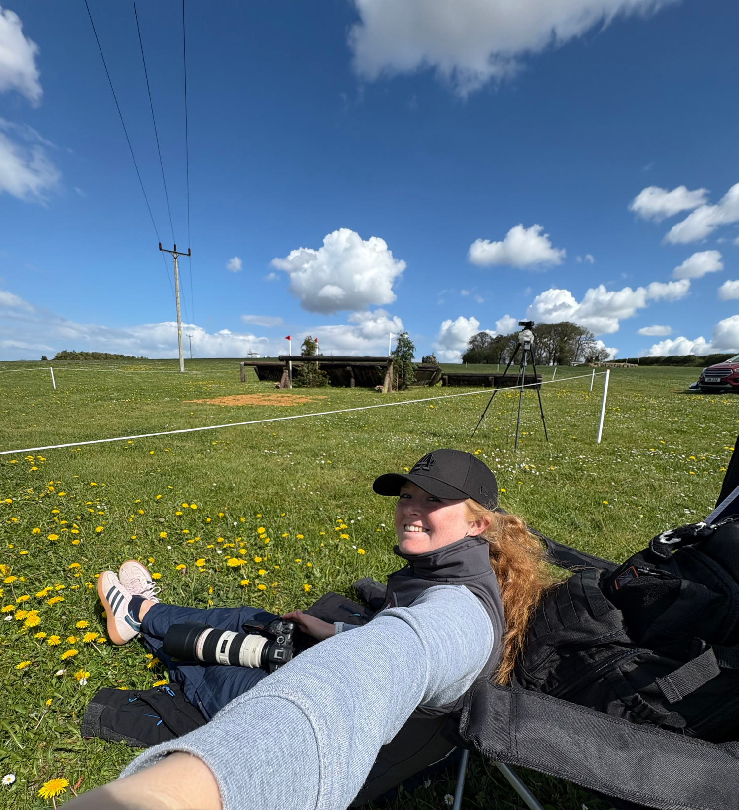 Young woman relaxing in folding chair with legs raised in sunny dandelion field at horse event.