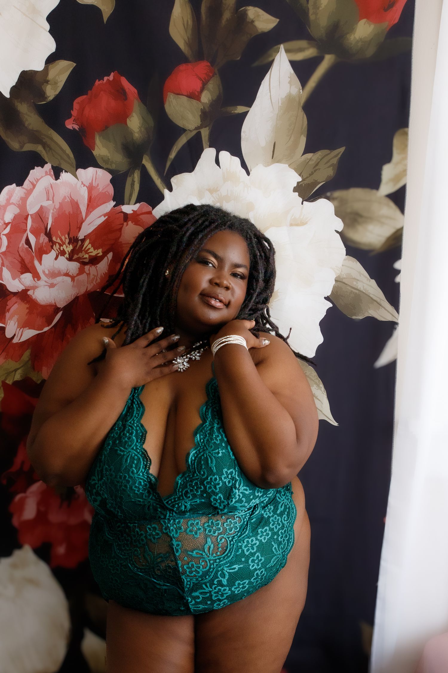 Plus-size woman posing confidently before a floral backdrop during a boudoir shoot with Nicole Fey Photography in Colorado Springs.