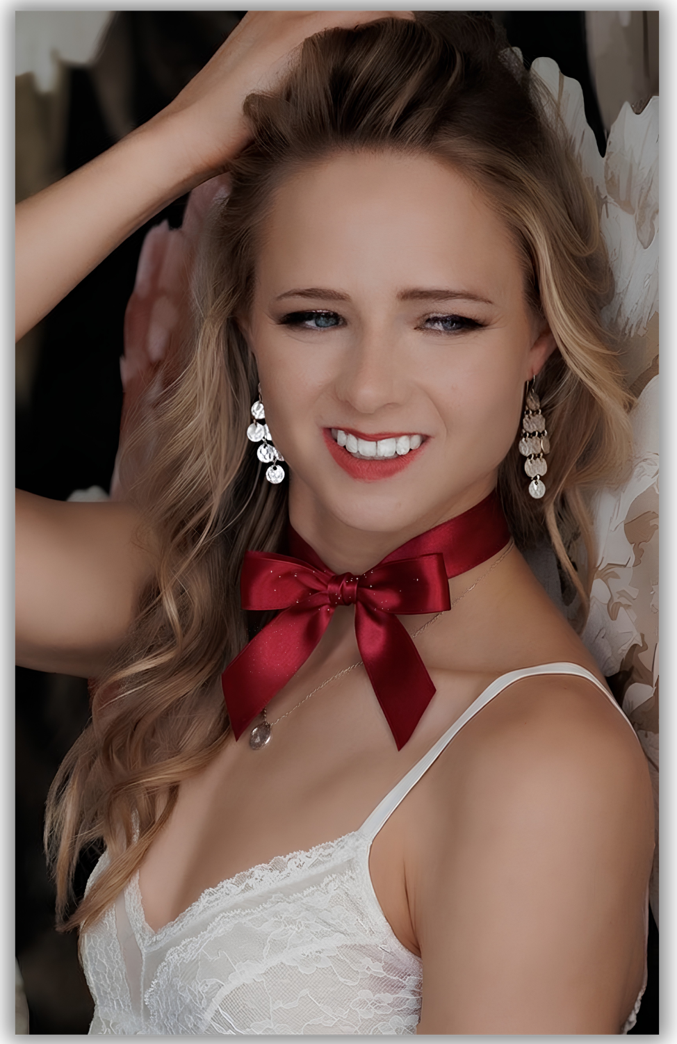 Young woman with blonde hair wearing a red satin Christmas bow choker and chandelier earrings smiling for boudoir in Colorado Springs .
