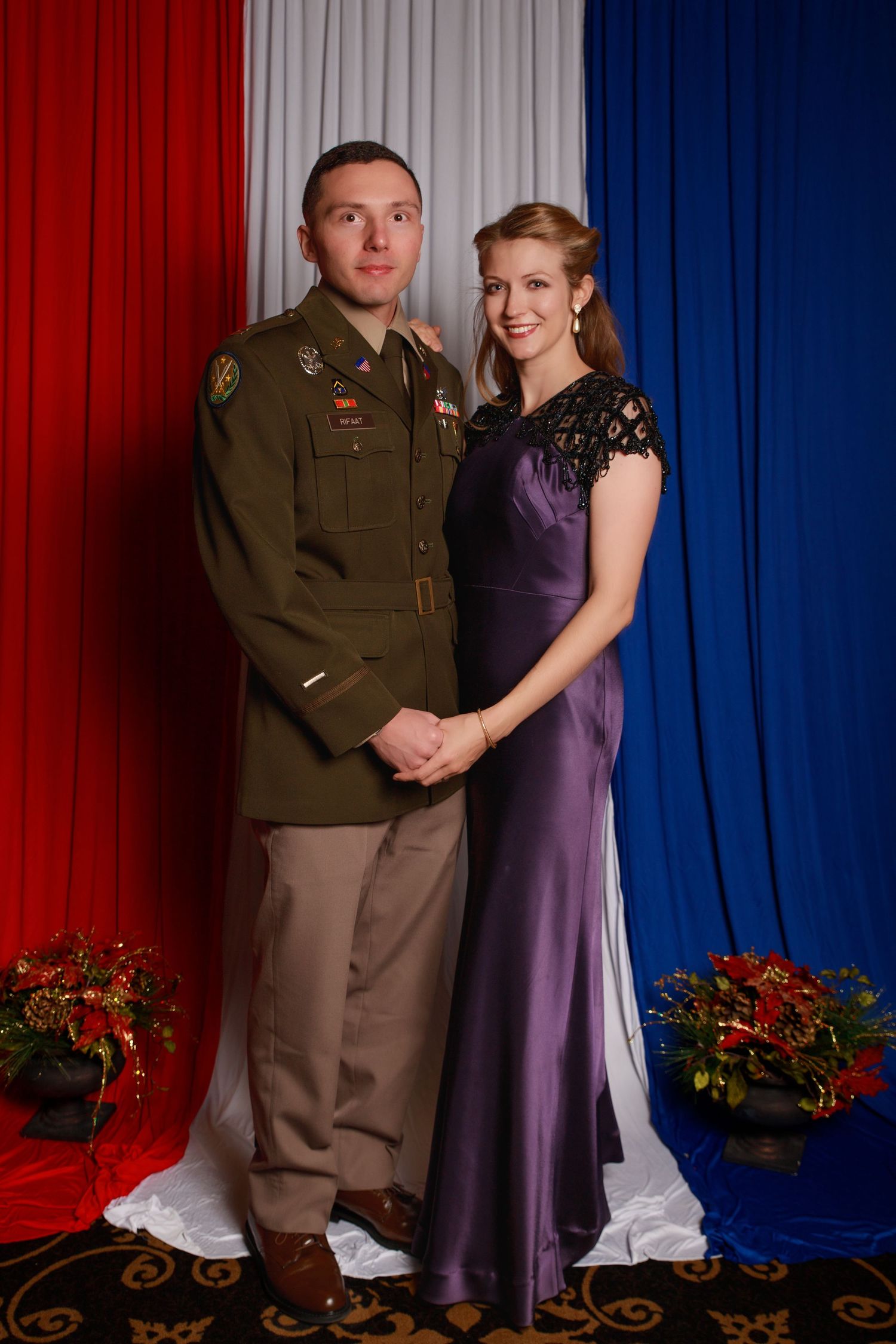 Military couple posing formally, man in olive Army uniform and woman in elegant purple satin gown.