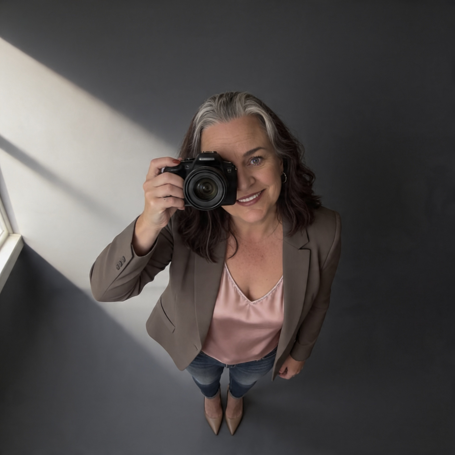Overhead view of a smiling woman with gray hair holding a camera up in a bright corner studio.