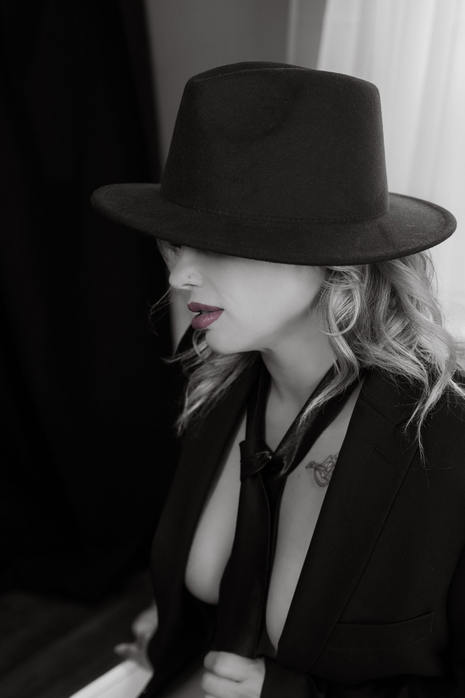 Black and white portrait of a blonde woman in a black fedora hat and blazer with red lips.